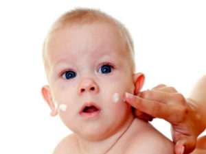 Младенцу мажут щечки кремом